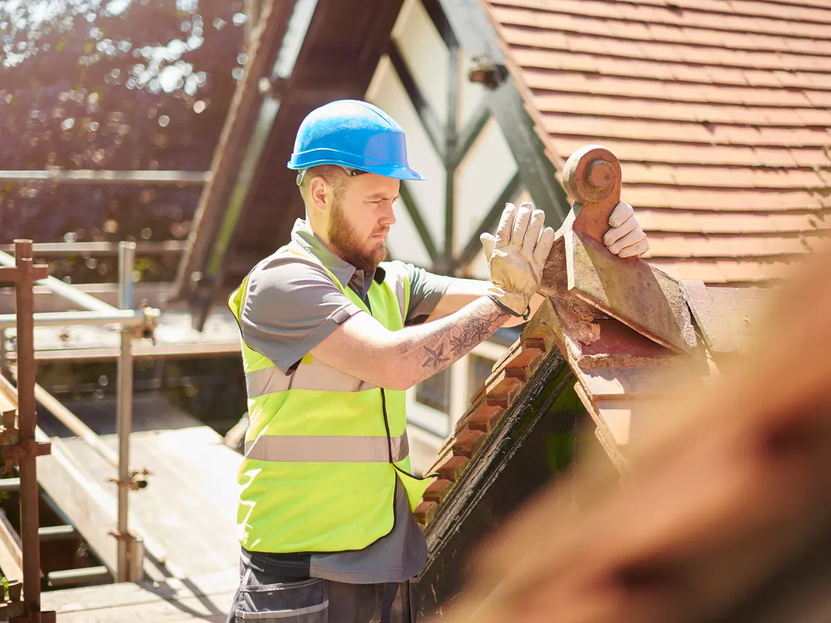 Roofer fitting a clay ridge tile from the scaffold