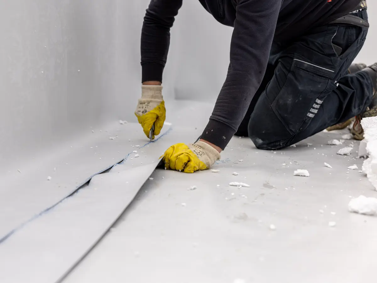 Roofer cutting single ply membrane on a flat roof