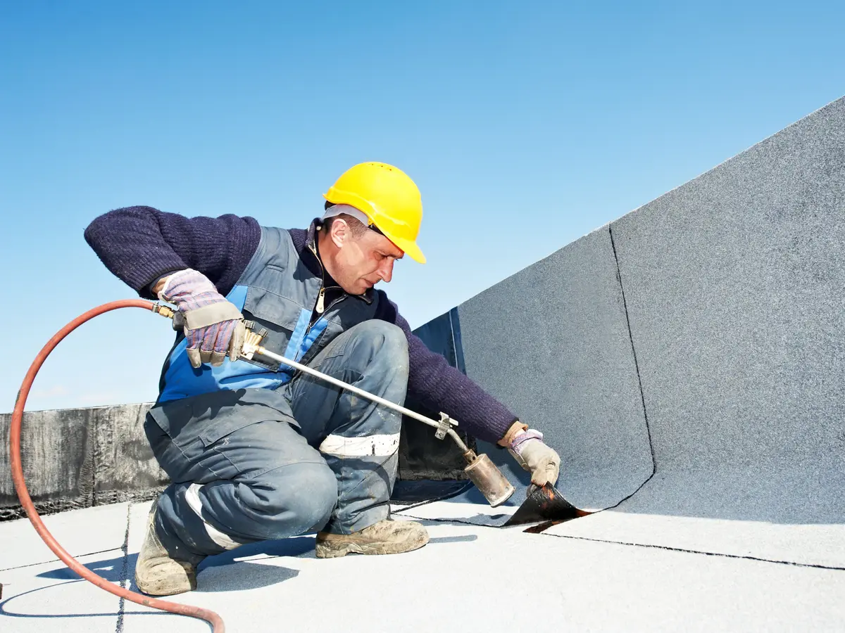 Roofer torch fixing felt to a flat roof upstand